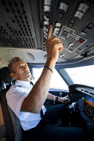Pilot completing an overhead-panel check in the cockpit