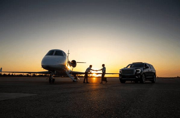 Two people meeting beside a private jet and waiting vehicle at sunset